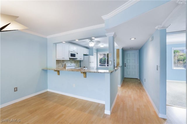 kitchen with light stone counters, a peninsula, white appliances, white cabinetry, and decorative columns