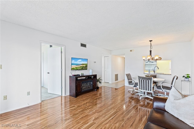 living room featuring light hardwood / wood-style flooring, a textured ceiling, sink, and an inviting chandelier