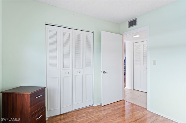 unfurnished bedroom with a textured ceiling, a closet, and light wood-type flooring