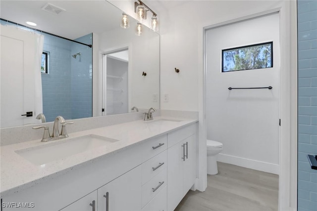 bathroom featuring hardwood / wood-style flooring, vanity, toilet, and tiled shower