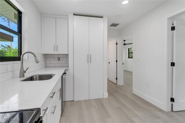 kitchen featuring backsplash, white cabinets, sink, light hardwood / wood-style flooring, and light stone counters