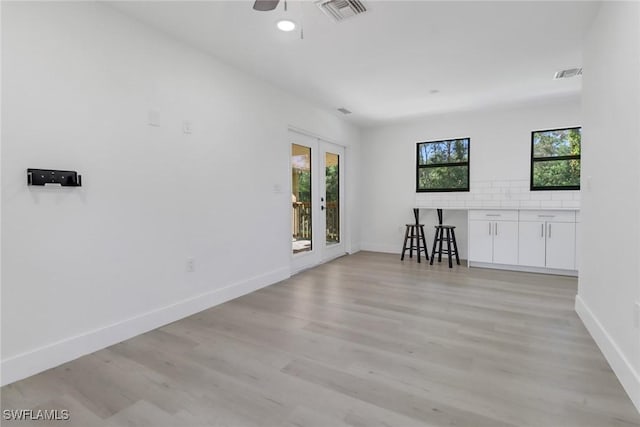 empty room with a wealth of natural light, french doors, ceiling fan, and light wood-type flooring