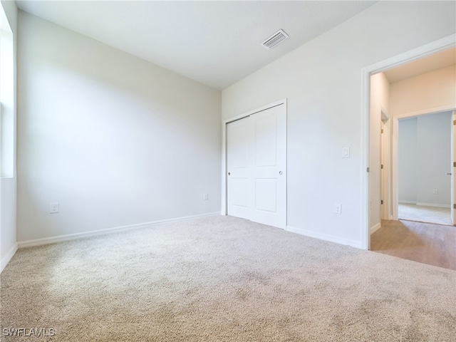 unfurnished bedroom with light colored carpet and a closet