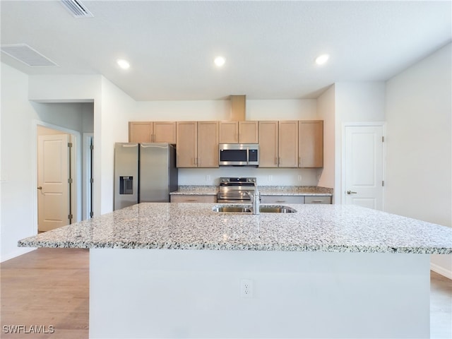 kitchen with light stone countertops, light hardwood / wood-style flooring, an island with sink, stainless steel appliances, and sink