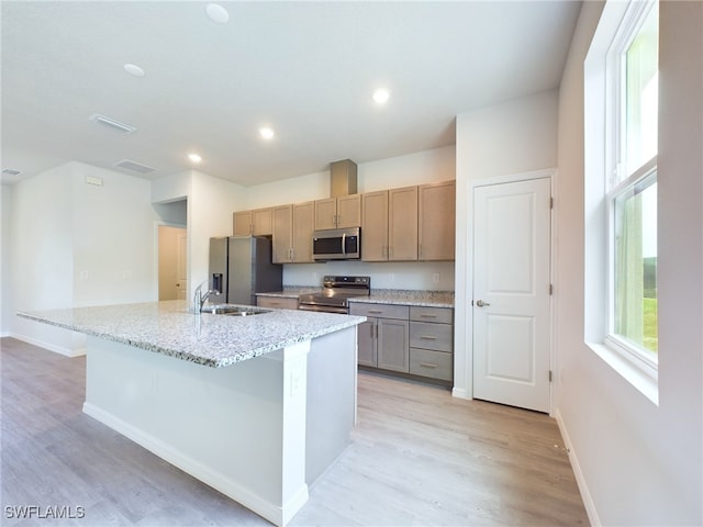 kitchen with light hardwood / wood-style flooring, appliances with stainless steel finishes, light stone counters, sink, and a center island with sink