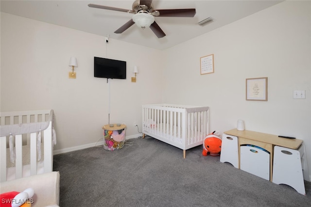 bedroom with a crib, dark colored carpet, and ceiling fan