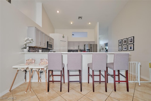 kitchen with kitchen peninsula, appliances with stainless steel finishes, decorative backsplash, gray cabinetry, and a breakfast bar