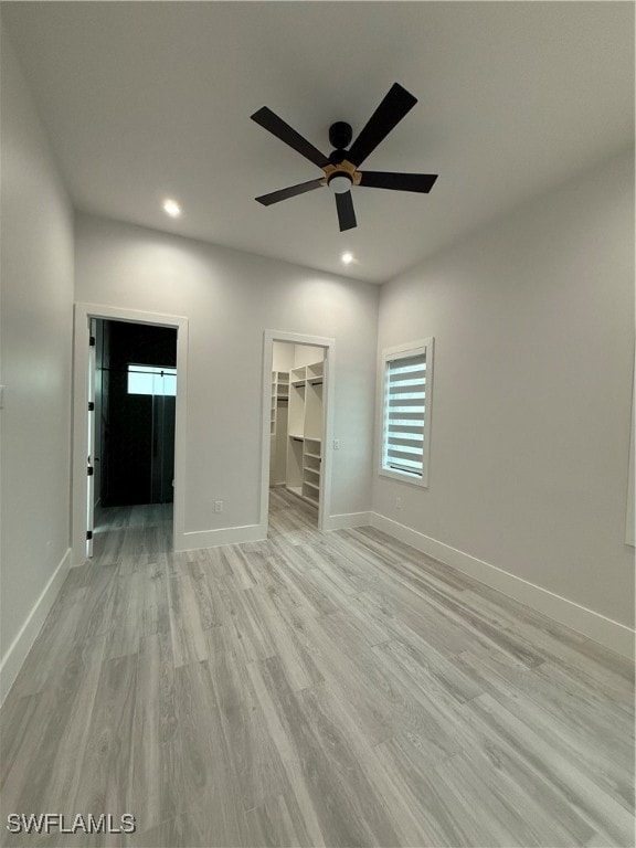 unfurnished bedroom featuring a walk in closet, ceiling fan, a closet, and light wood-type flooring