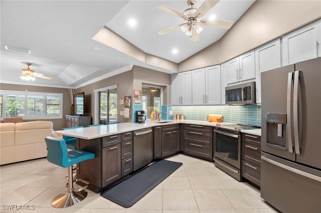 kitchen featuring kitchen peninsula, appliances with stainless steel finishes, a breakfast bar area, white cabinets, and ornamental molding