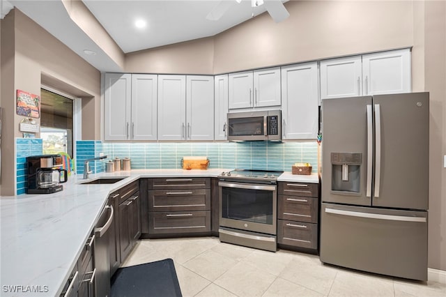 kitchen with appliances with stainless steel finishes, backsplash, light stone counters, sink, and lofted ceiling