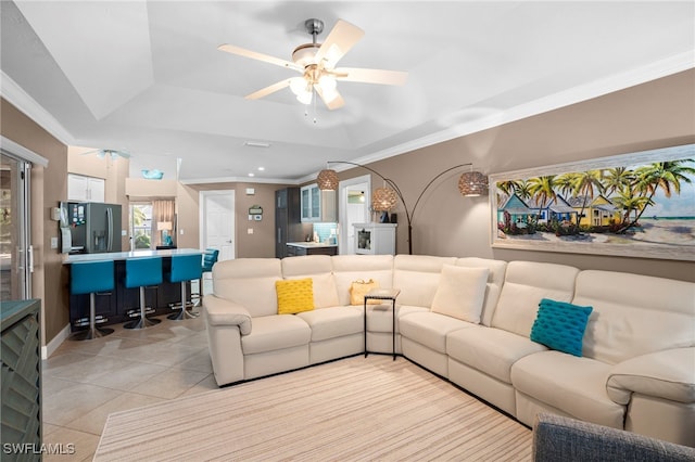 living room with light tile patterned floors, a raised ceiling, ceiling fan, and ornamental molding