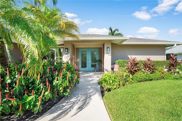 view of exterior entry with stucco siding, a yard, and french doors