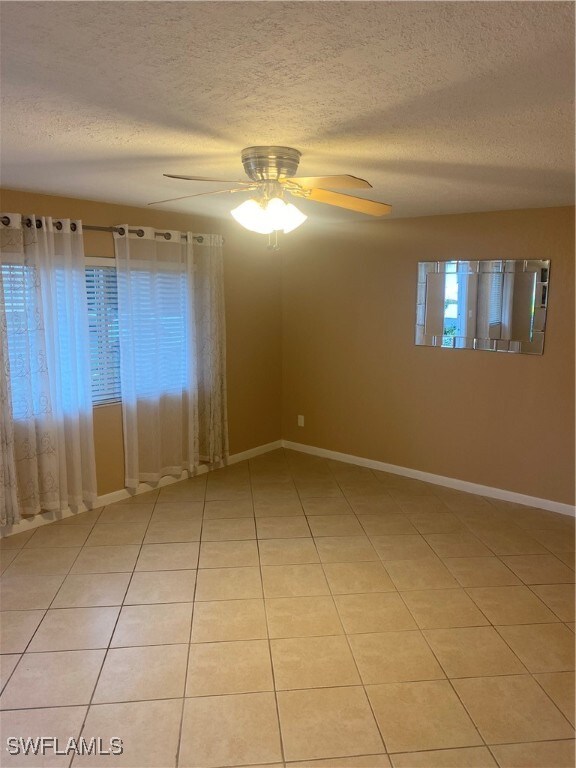 empty room with a textured ceiling, ceiling fan, and light tile patterned floors