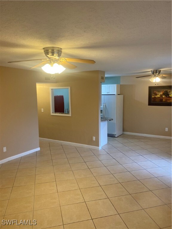 empty room featuring a textured ceiling, ceiling fan, and light tile patterned floors