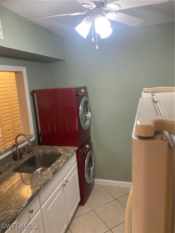 laundry room with ceiling fan, light tile patterned floors, stacked washer / drying machine, and sink