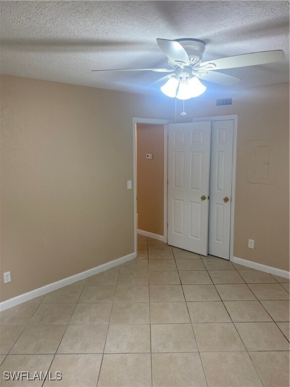 spare room featuring a textured ceiling, light tile patterned floors, and ceiling fan