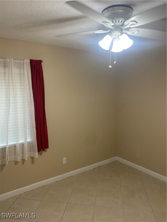 empty room featuring ceiling fan, light tile patterned floors, and a textured ceiling