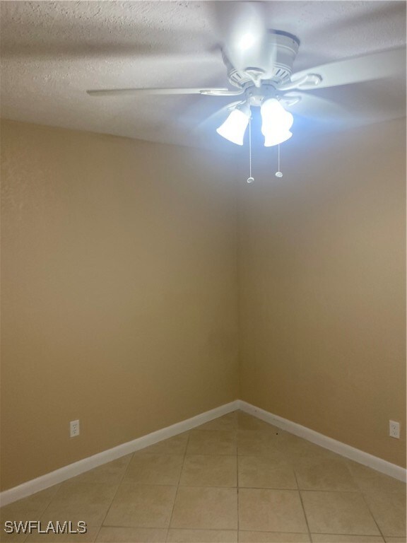 spare room featuring ceiling fan, light tile patterned floors, and a textured ceiling