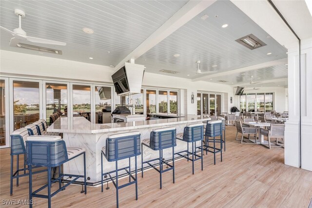 kitchen with a kitchen bar, ceiling fan, light stone countertops, and light wood-type flooring