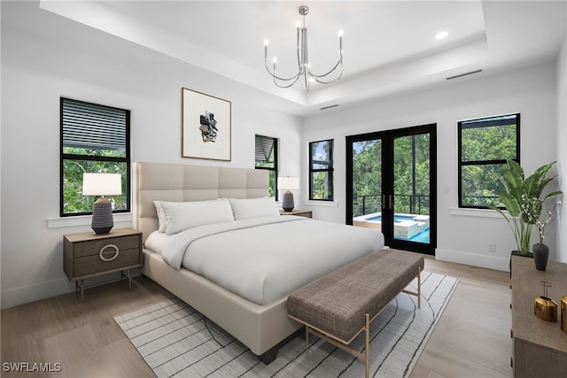 bedroom with multiple windows, a tray ceiling, hardwood / wood-style flooring, and access to outside