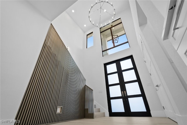 foyer entrance featuring a towering ceiling, french doors, hardwood / wood-style floors, and a notable chandelier