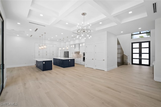 unfurnished living room with coffered ceiling, a notable chandelier, beamed ceiling, and light wood-type flooring