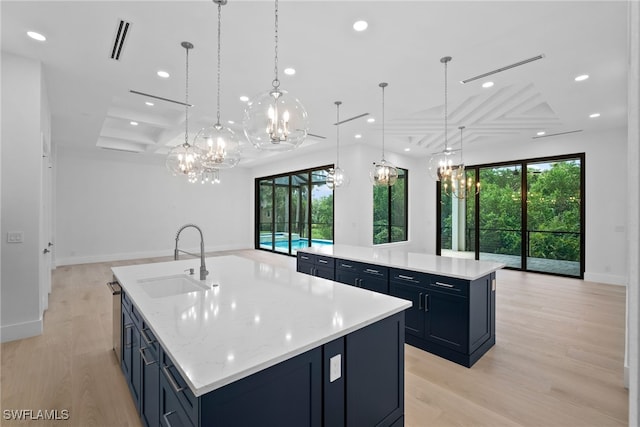 kitchen featuring hanging light fixtures, light wood-type flooring, light stone counters, a large island with sink, and sink