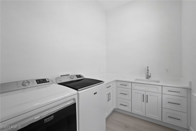 laundry area featuring washing machine and clothes dryer, cabinets, sink, and light hardwood / wood-style floors