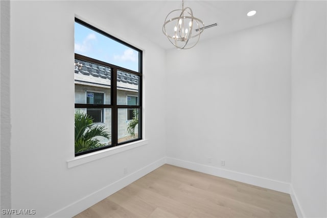 spare room with a wealth of natural light, light hardwood / wood-style flooring, and a notable chandelier