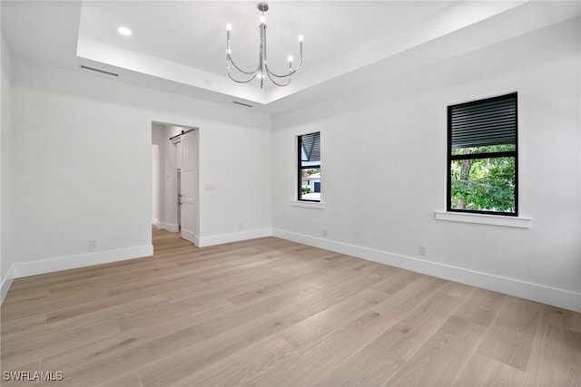 empty room with light hardwood / wood-style floors, plenty of natural light, a raised ceiling, and a chandelier