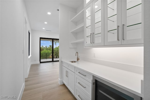 bar with light hardwood / wood-style flooring, white cabinets, wine cooler, and sink