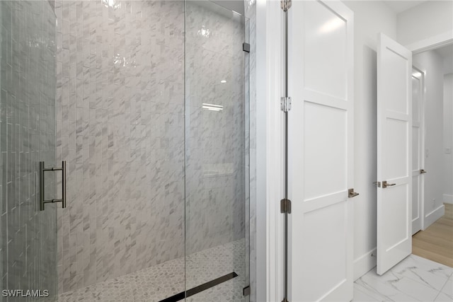 bathroom featuring marble finish floor, a shower stall, and baseboards