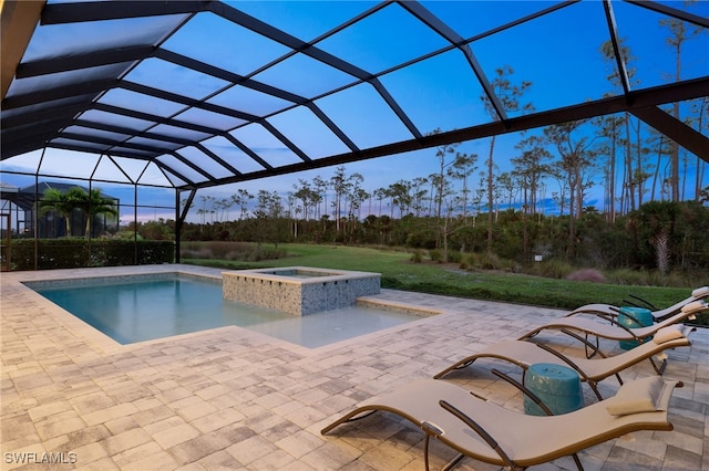 pool at dusk featuring a patio, a lanai, and an in ground hot tub