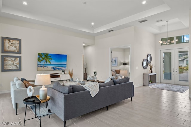 living room with french doors, light hardwood / wood-style flooring, a notable chandelier, and a tray ceiling