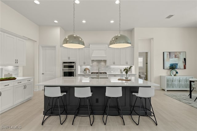 kitchen with a center island with sink, white cabinetry, decorative light fixtures, decorative backsplash, and double oven