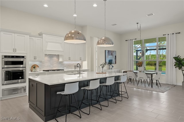 kitchen featuring appliances with stainless steel finishes, pendant lighting, sink, white cabinets, and a kitchen island with sink