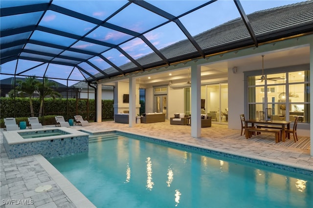 pool at dusk with a lanai, outdoor lounge area, a patio, and an in ground hot tub