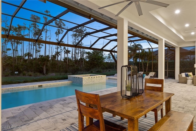 pool at dusk featuring a lanai, ceiling fan, a patio, and an in ground hot tub