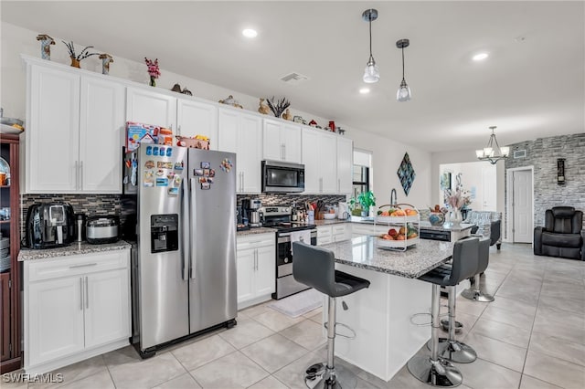 kitchen with decorative light fixtures, appliances with stainless steel finishes, a breakfast bar, white cabinetry, and light stone counters