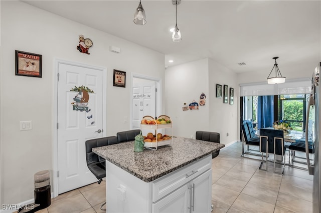 kitchen featuring light tile patterned floors, a center island, light stone counters, white cabinetry, and pendant lighting