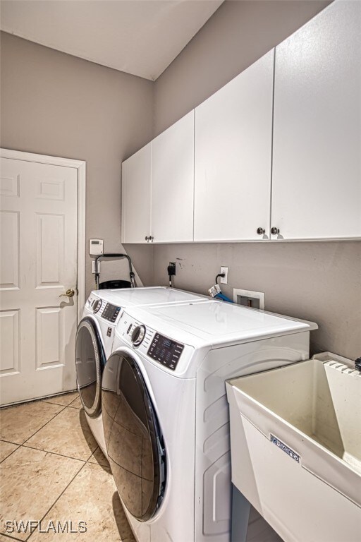 laundry area featuring separate washer and dryer, light tile patterned floors, cabinets, and sink