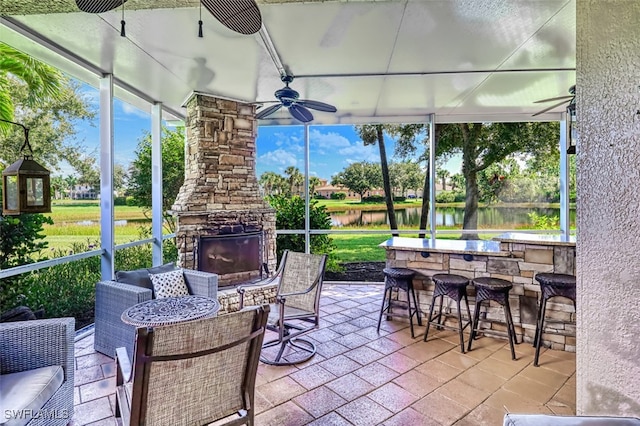 sunroom / solarium with an outdoor stone fireplace, ceiling fan, and a water view