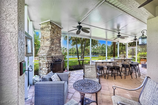 view of patio featuring outdoor dry bar, glass enclosure, a water view, and a ceiling fan