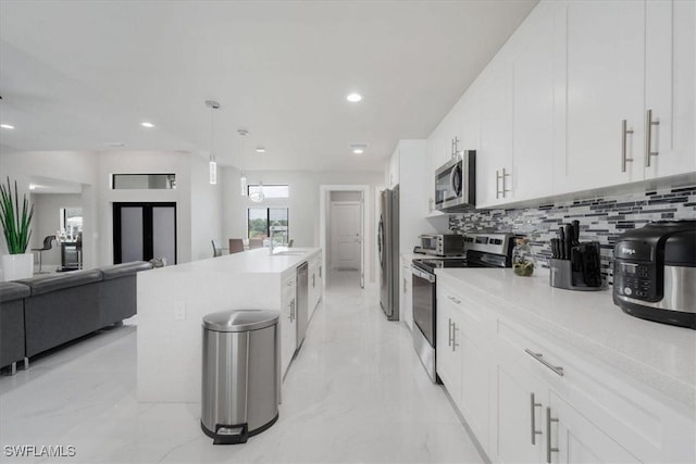 kitchen featuring stainless steel appliances, white cabinetry, sink, an island with sink, and tasteful backsplash