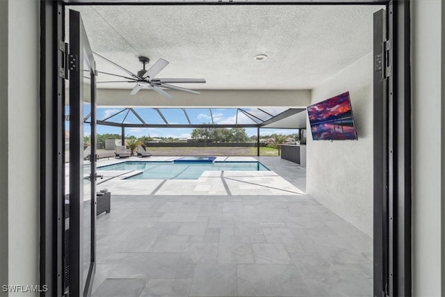 view of pool featuring glass enclosure, ceiling fan, and a patio area