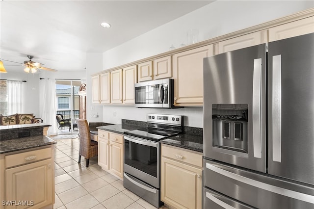 kitchen featuring light tile patterned flooring, ceiling fan, stainless steel appliances, and dark stone countertops