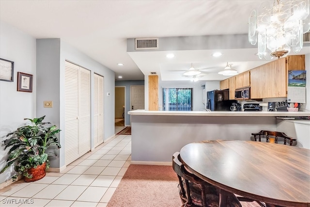 kitchen featuring light brown cabinets, kitchen peninsula, hanging light fixtures, light tile patterned floors, and black fridge