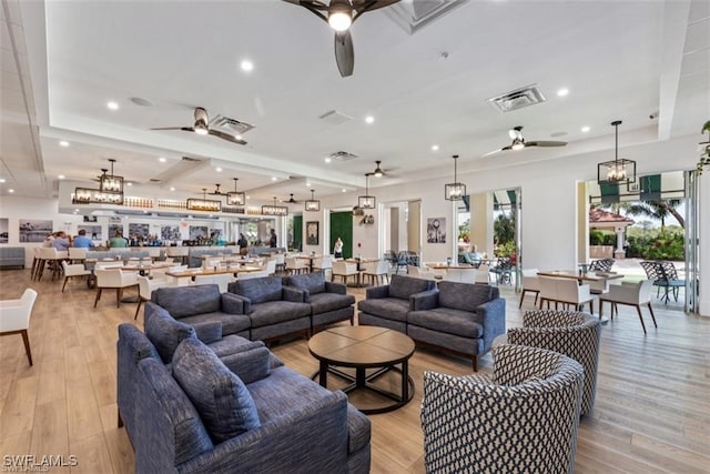 living room featuring ceiling fan with notable chandelier and light wood-type flooring