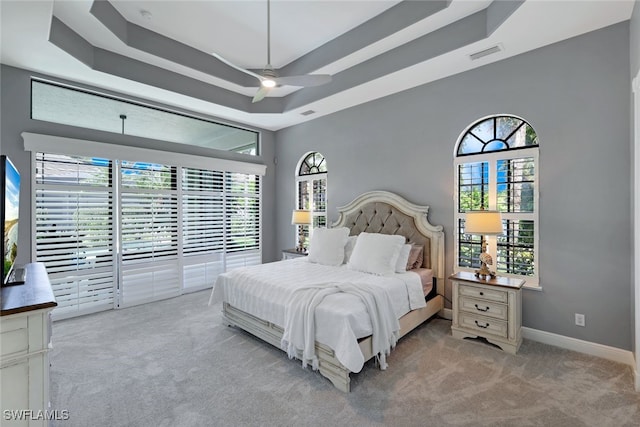 carpeted bedroom with a tray ceiling, multiple windows, access to exterior, and ceiling fan