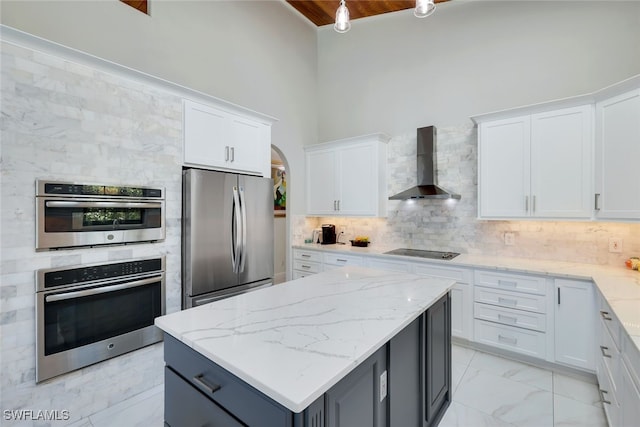 kitchen featuring a high ceiling, stainless steel appliances, white cabinets, and wall chimney range hood